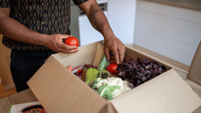 Man delightedly opening a box full of fresh vegetables, experiencing one of the best meal delivery kits in Canada.