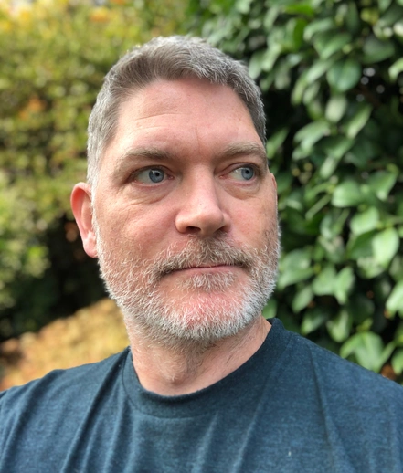 Josh Malcolm, creator and curator of The Quick Dish recipe website, outdoors with a natural greenery background.