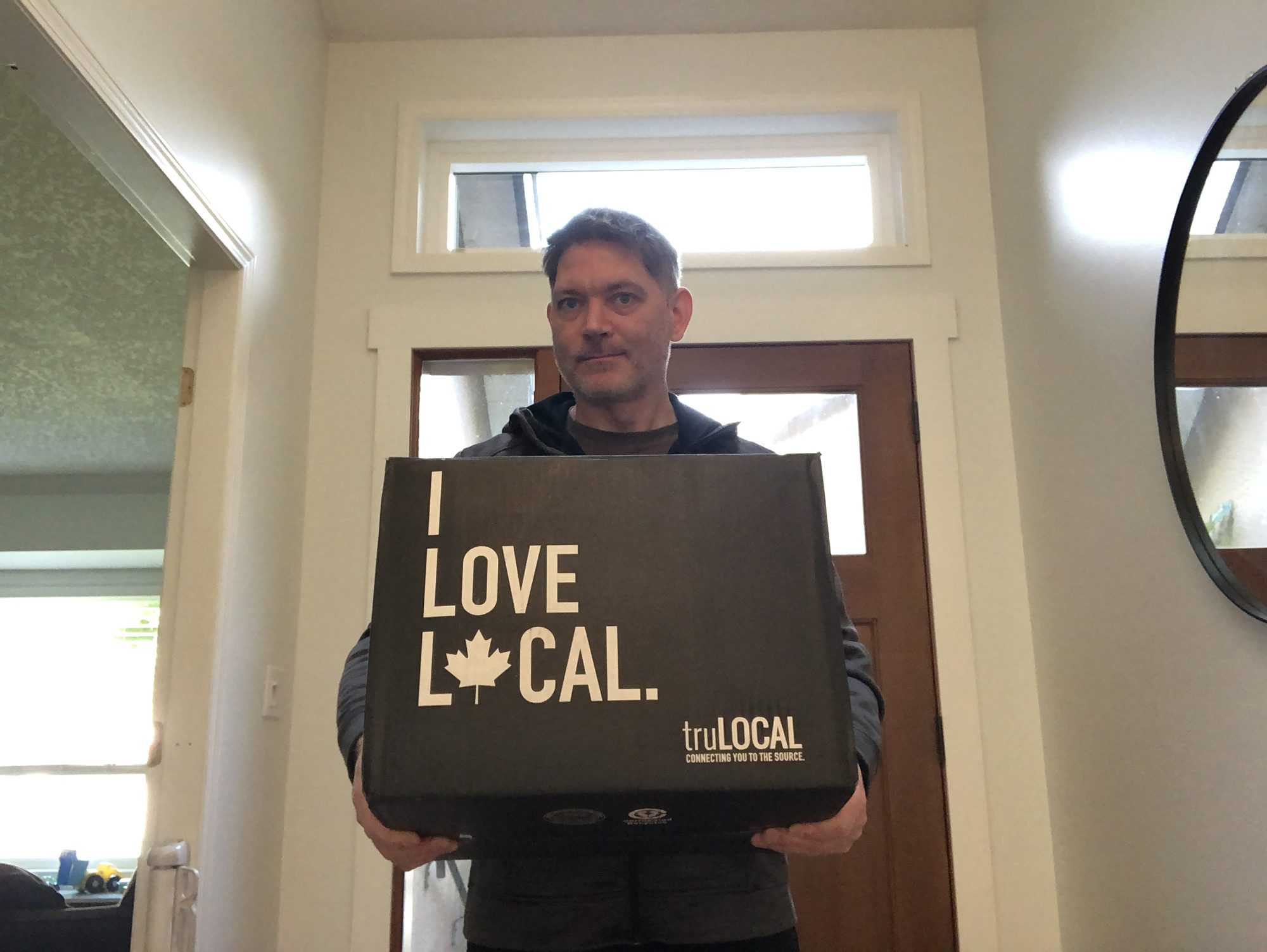 The Quick Dish reviewer holding the truLOCAL meat delivery box at the front door.